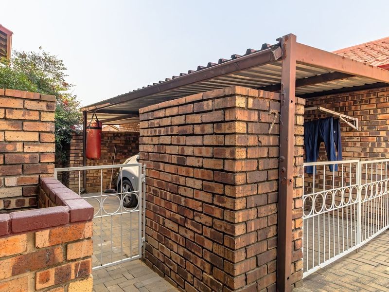 Rear exterior area featuring a brick-walled carport, paved driveway, and secure metal gate access to the property.