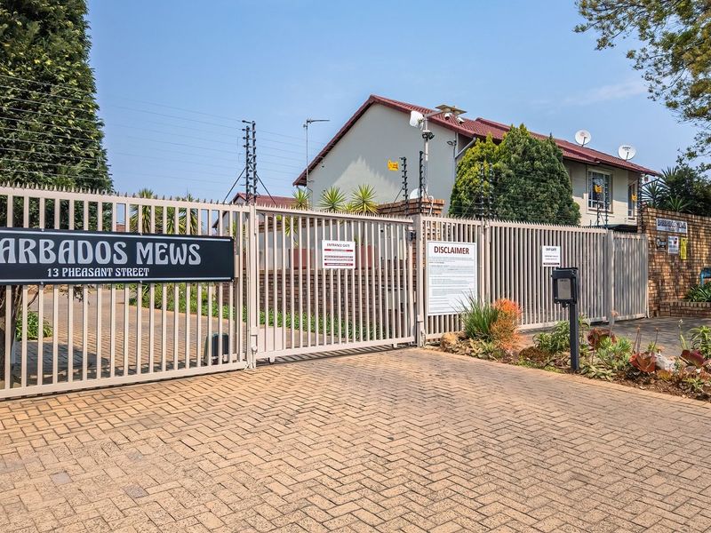 Front entrance view of Barbados Mews townhouse complex, featuring secure gated access, paved driveway, and perimeter electric fencing.