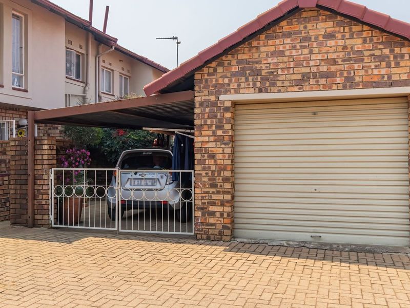 A townhouse exterior featuring a brick-faced single garage with a roller shutter door and an adjacent covered carport area.