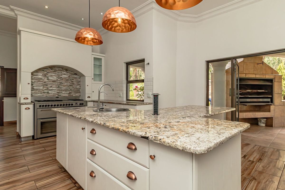 Modern kitchen featuring a large granite island, built-in oven with extractor, and seamless flow to an outdoor patio area with a built-in braai.