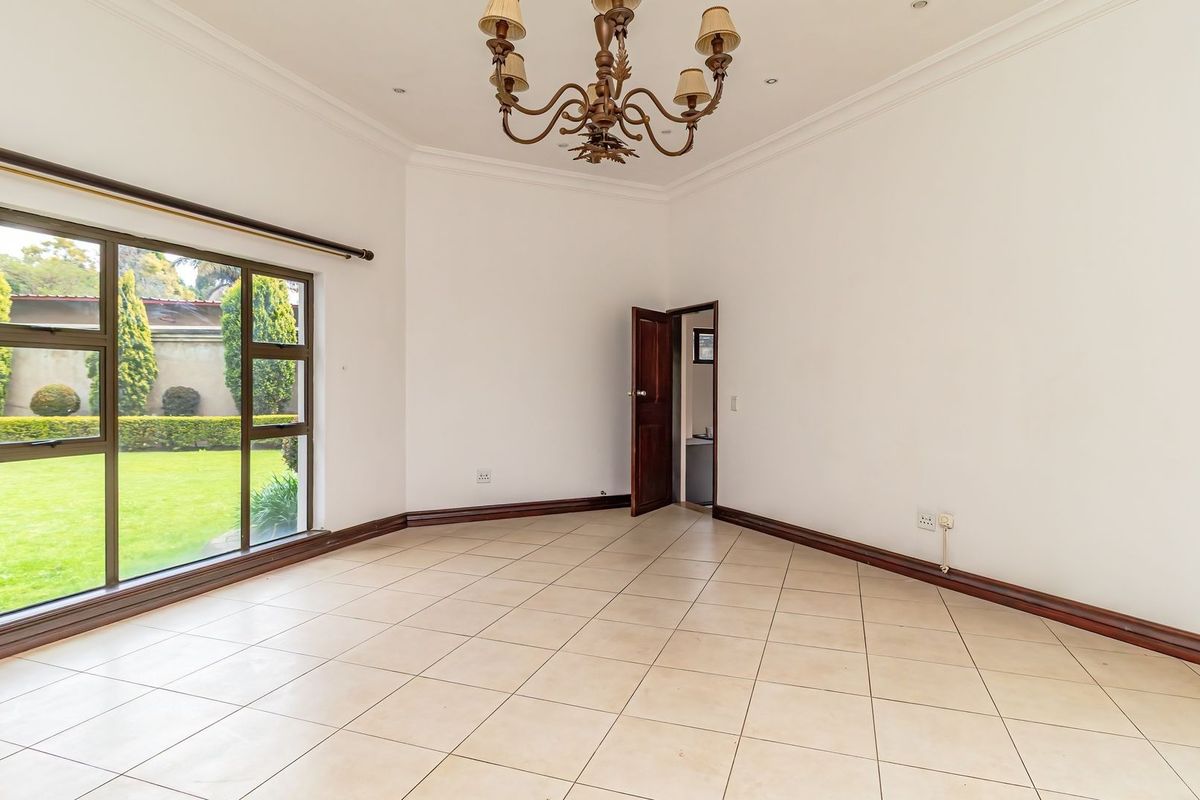 A bright and spacious empty living room featuring neutral tiled flooring, crown molding, and a large window overlooking the garden.