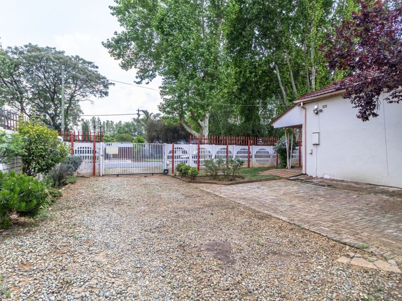 Front exterior view featuring a gravel driveway, paved walkway, and secure perimeter fencing with gated access to the property.