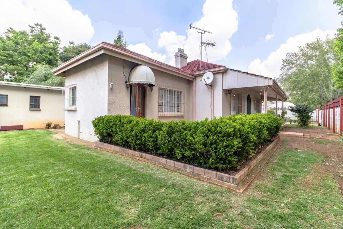 Rear view of the house featuring a tiled roof, security bars on windows, and a landscaped garden area with brick edging.