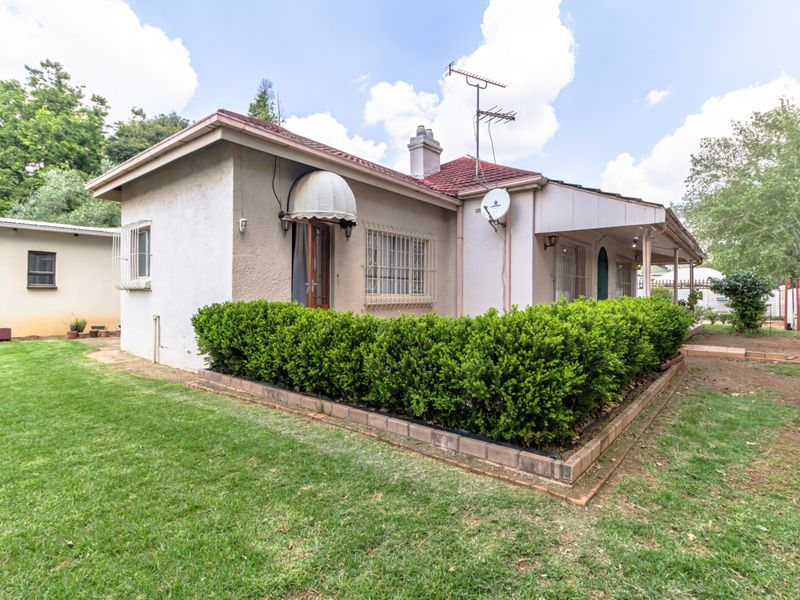 Rear view of the house featuring a tiled roof, security bars on windows, and a landscaped garden area with brick edging.