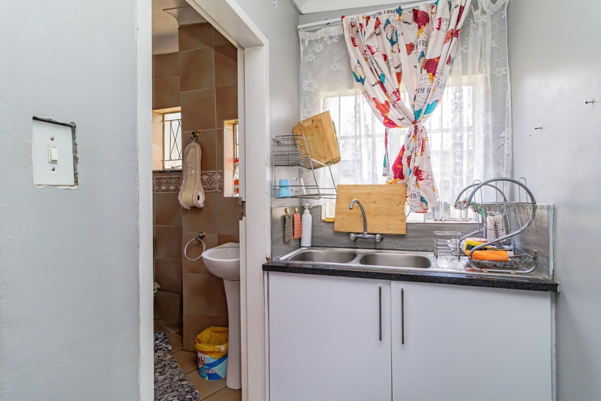 A compact kitchen area featuring a double sink and built-in cabinetry, with an adjacent bathroom visible through the doorway.