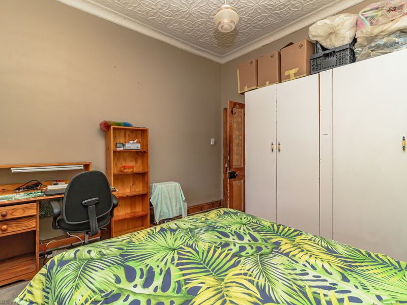 A bedroom featuring a classic pressed metal ceiling, built-in storage cupboards, and a timber door, offering a functional space with period character.