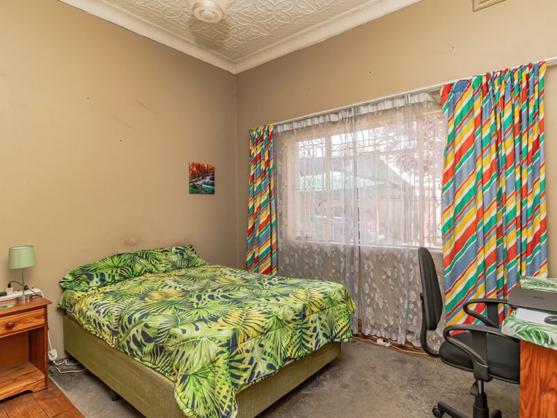 A bedroom featuring an ornate pressed metal ceiling and a window fitted with security bars, requiring cosmetic updates to the walls and flooring.