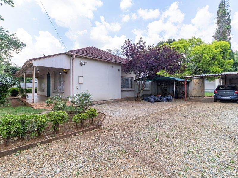 Front view of the house featuring a paved driveway, covered patio, carport, and established garden area.
