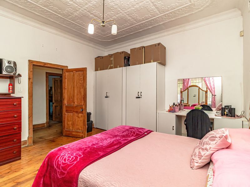 Spacious bedroom featuring original pressed metal ceilings, timber flooring, and built-in wardrobe storage, offering a classic character aesthetic with potential for cosmetic updates.