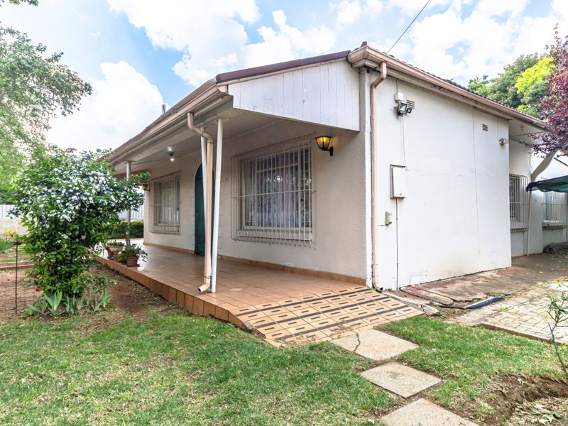 Rear view of the property featuring a covered tiled patio, security bars on windows, and a paved walkway leading to the garden area.