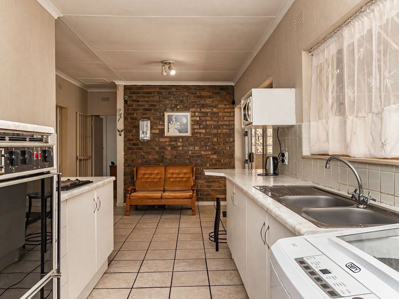 A functional kitchen featuring a built-in oven, double sink, laminate countertops, and a distinctive exposed brick feature wall with tiled flooring throughout.
