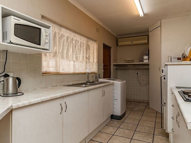 Functional scullery area featuring built-in cabinetry, laminate countertops, a stainless steel sink, and tiled flooring, providing additional prep and utility space.
