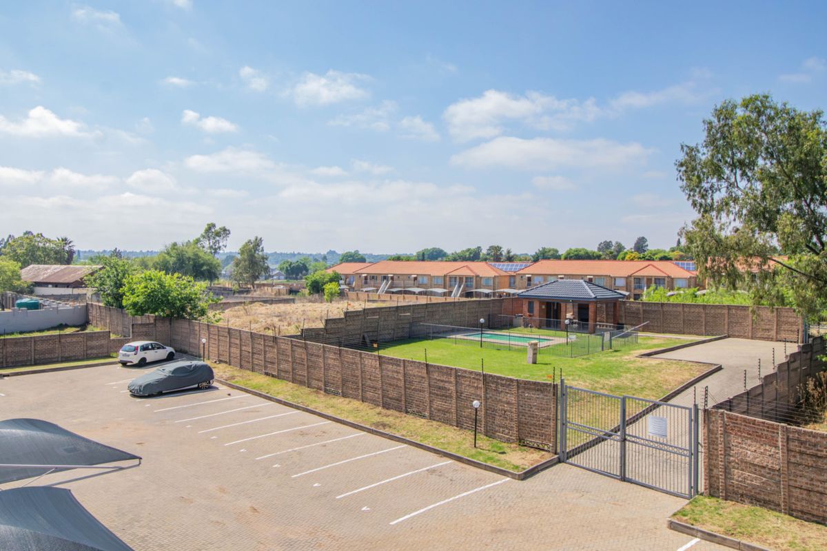 Aerial view of the apartment complex grounds featuring a communal swimming pool, clubhouse, paved parking area, and secure perimeter walling.