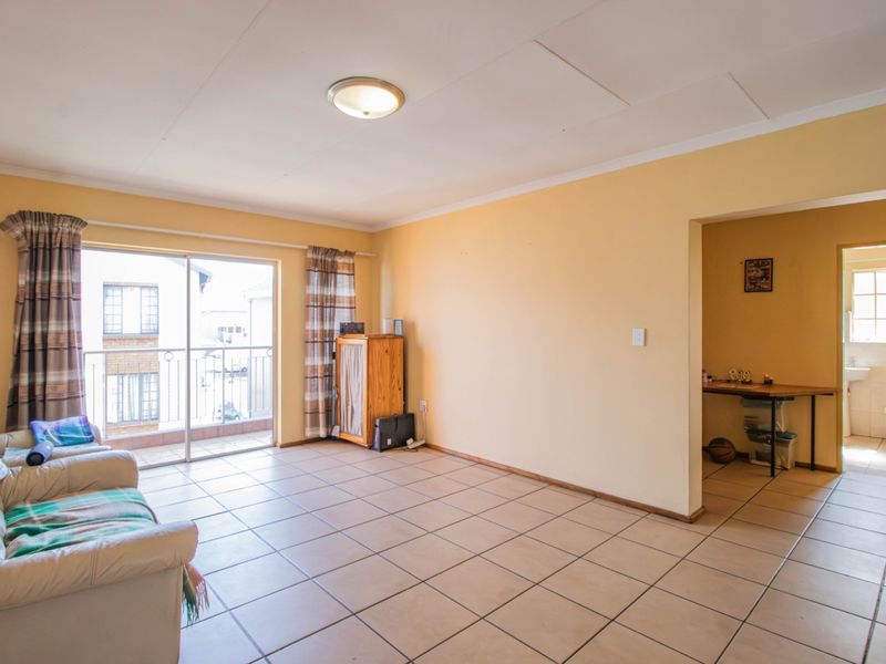 A living room featuring tiled flooring and a sliding glass door leading to a balcony, with an adjacent view into a bathroom area.