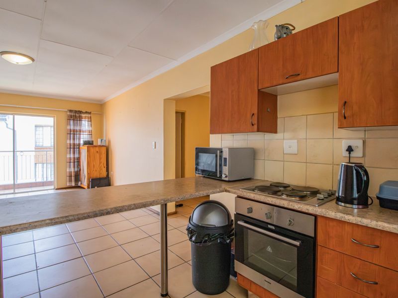 Open-plan kitchen featuring wooden cabinetry, laminate countertops, and tiled flooring, flowing into a living area with direct access to a balcony.
