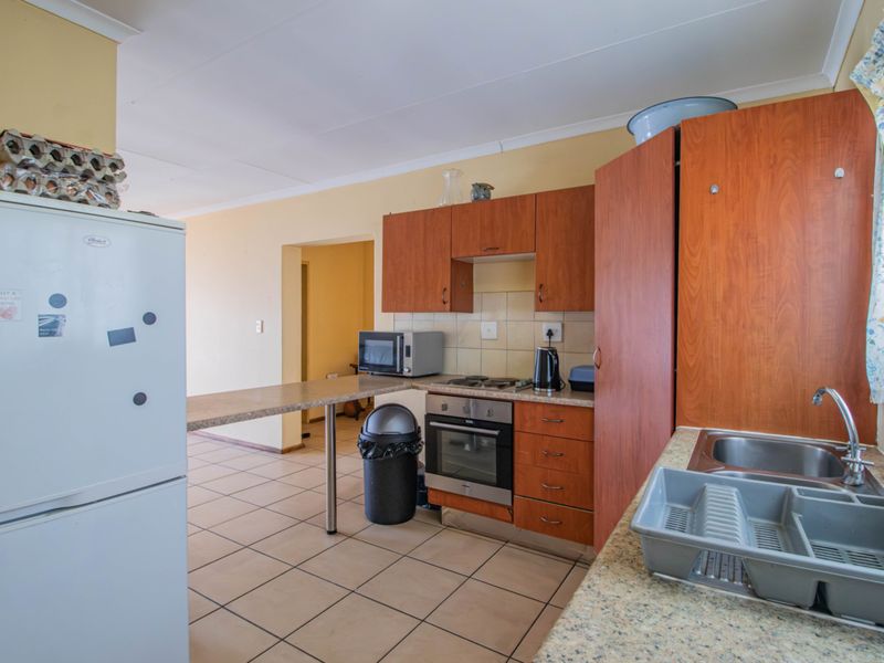 A functional kitchen featuring wood-finish cabinetry, laminate countertops, a built-in oven and hob, and a breakfast bar, with tiled flooring throughout.
