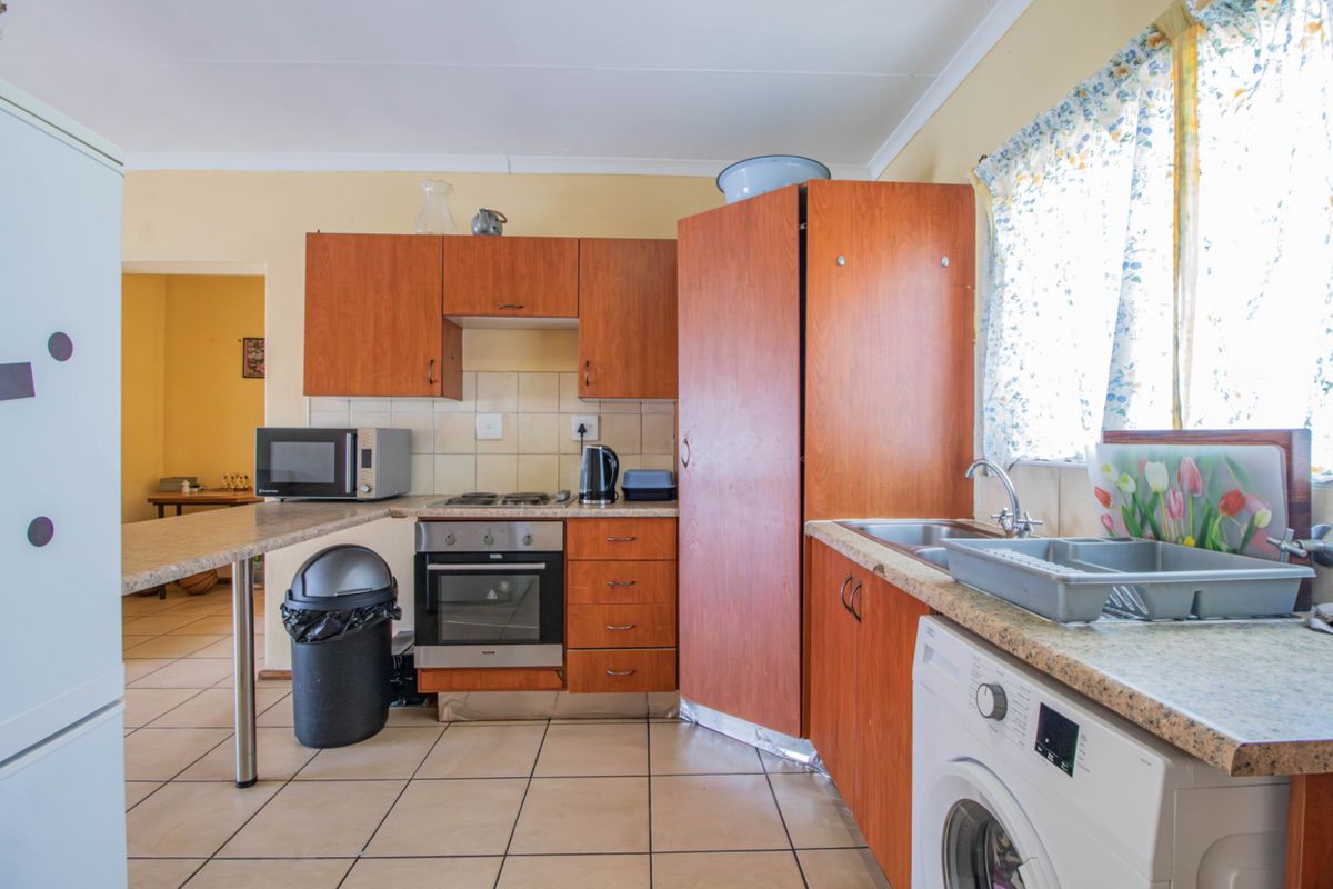 A functional kitchen featuring wood-look laminate cabinetry, tiled flooring, a built-in oven, and a stainless steel sink with a tiled backsplash.