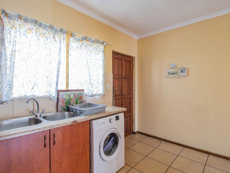 A functional kitchen area featuring wooden cabinetry, double basin sink, tiled flooring, and direct access to an exterior door.