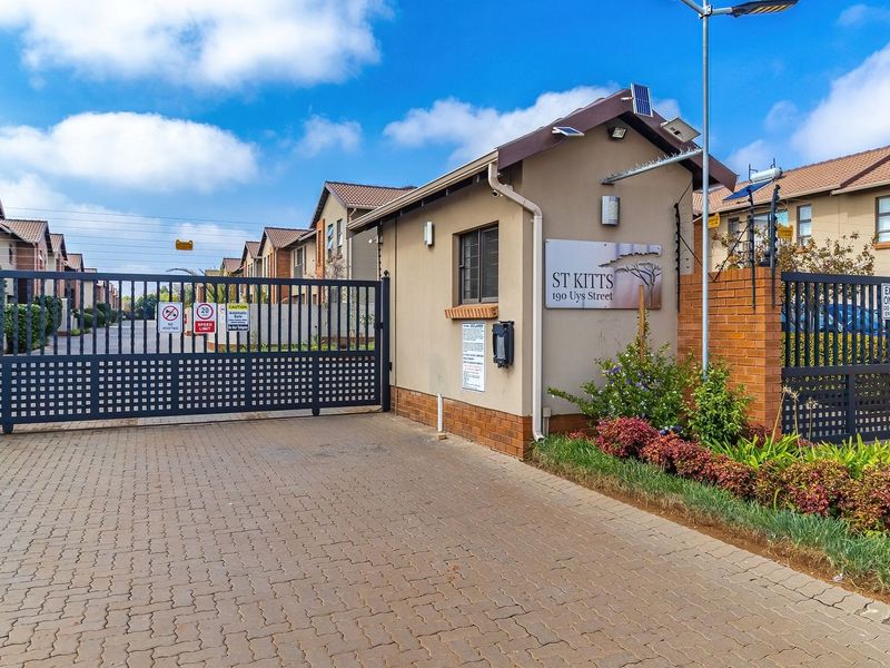 The secure entrance to St Kitts townhouse complex, featuring a gated access point, guard house, and well-maintained paved driveway and perimeter fencing.