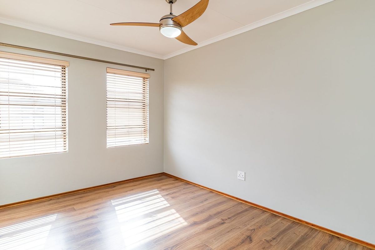 A bright, empty bedroom featuring laminate flooring, built-in cupboards, and a modern ceiling fan, offering a clean and neutral space ready for personalization.