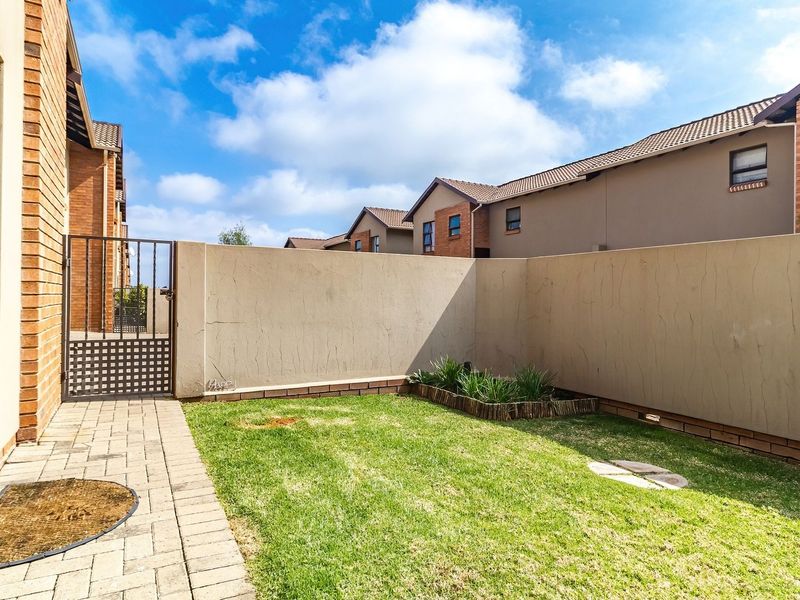 A private rear garden featuring a paved patio area, a small lawn, and a secure metal gate enclosed by a boundary wall.
