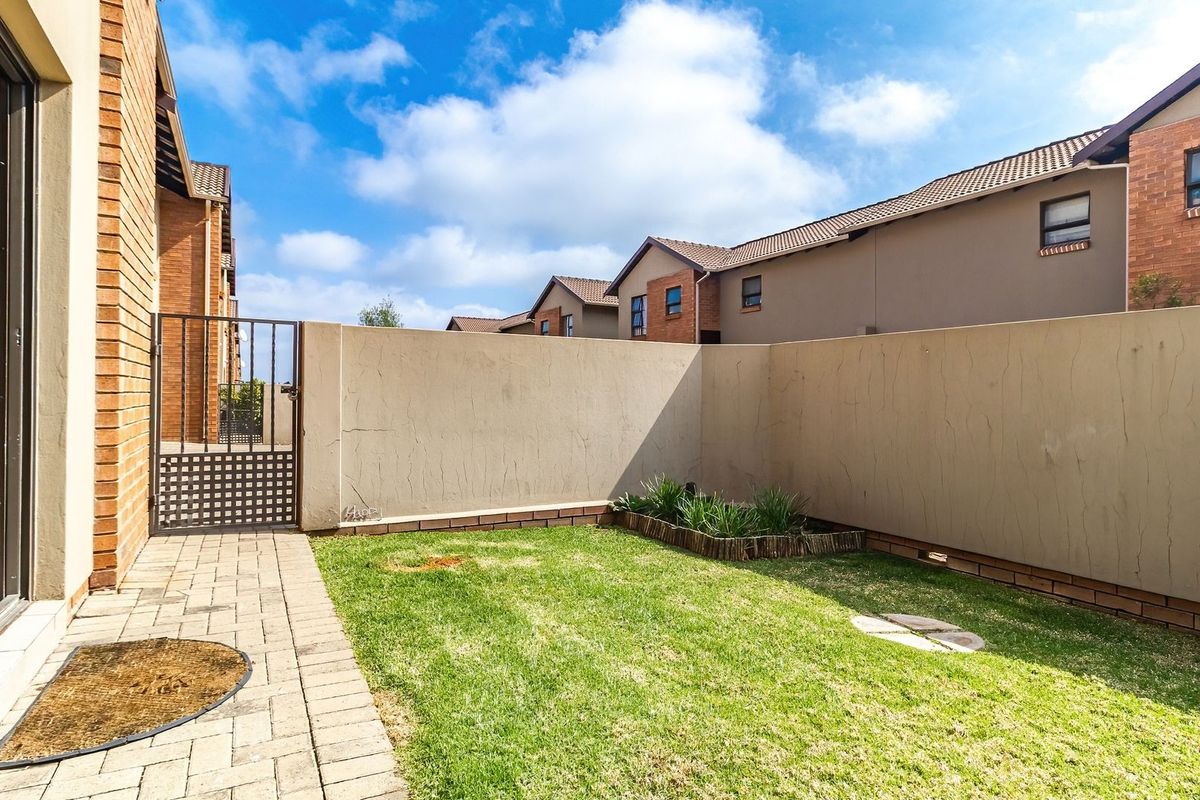 A private rear garden featuring a paved patio area, a small lawn, and a secure metal gate enclosed by a boundary wall.