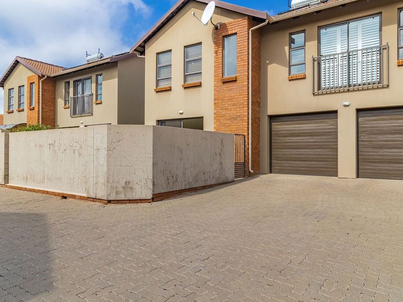 Front elevation of a townhouse complex featuring a paved driveway, double garage doors, and a private balcony with a boundary wall.