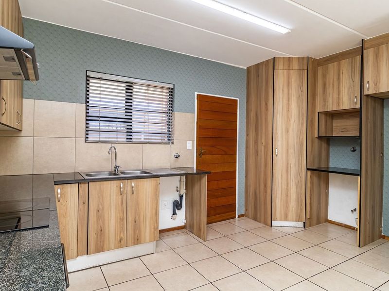 A functional kitchen featuring wood-look cabinetry, dark laminate countertops, a double basin sink, and tiled flooring, offering a clean and practical workspace.