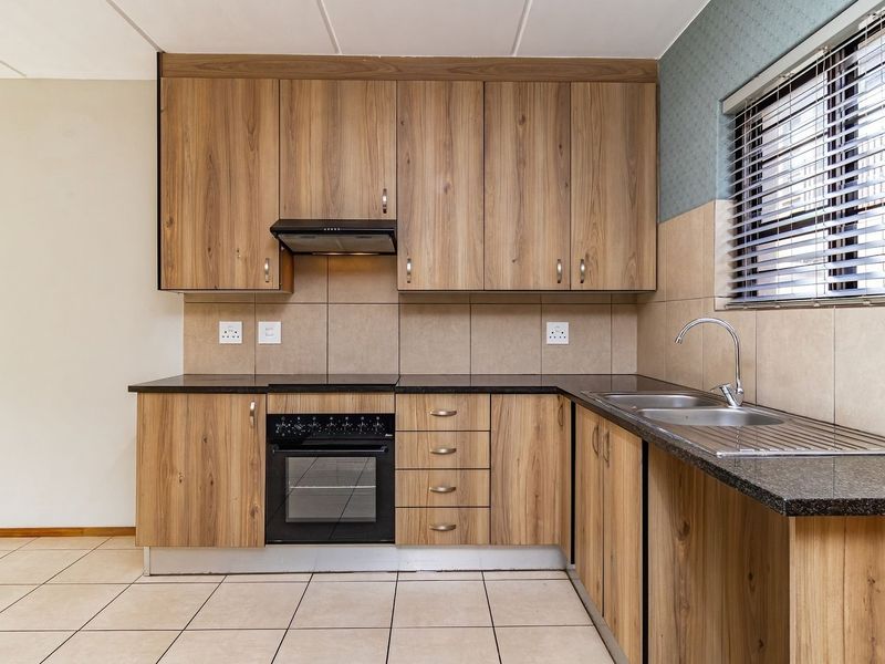 A clean, functional kitchen featuring wood-look laminate cabinetry, granite countertops, built-in oven, hob, and extractor fan with neutral tiled flooring and backsplash.