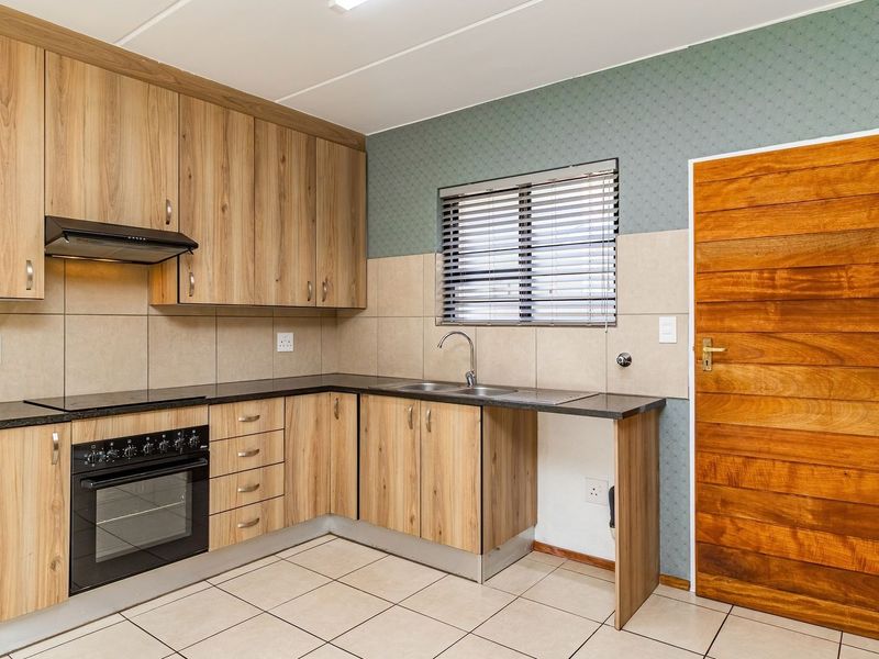 A clean, functional kitchen featuring wood-look laminate cabinetry, granite countertops, a built-in oven with extractor fan, and neutral tiled flooring.