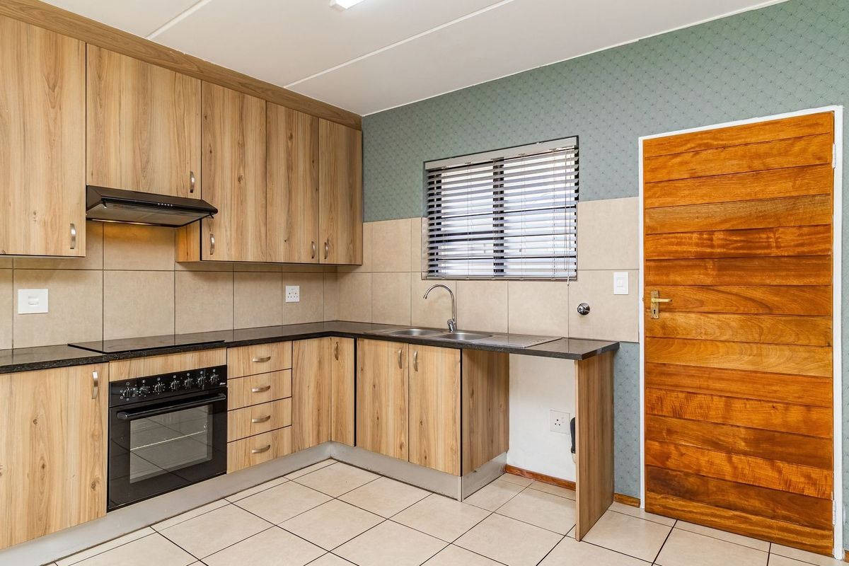 A clean, functional kitchen featuring wood-look laminate cabinetry, granite countertops, a built-in oven with extractor fan, and neutral tiled flooring.