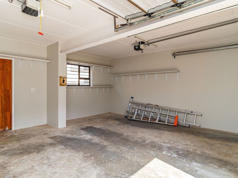 A spacious, clean double garage featuring concrete flooring, built-in wall shelving, and an automated garage door motor.