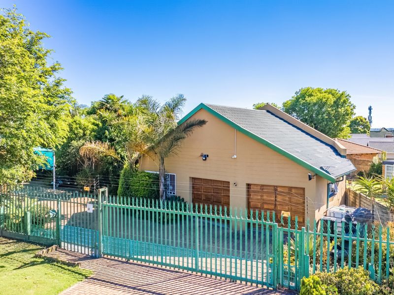 Front view of the property featuring a double garage, secure metal gate, and paved driveway with perimeter electric fencing.