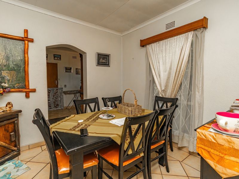 A dining area featuring tiled flooring and an arched doorway leading to an adjacent room, with a window dressed in curtains.
