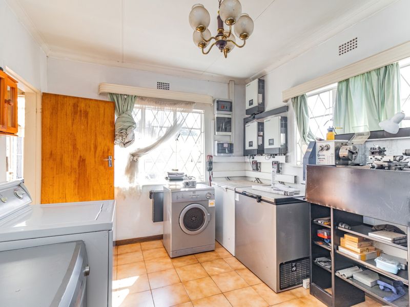 Functional laundry room featuring tiled flooring, built-in electrical infrastructure, and security bars on windows, offering potential for modernization and improved utility space organization.
