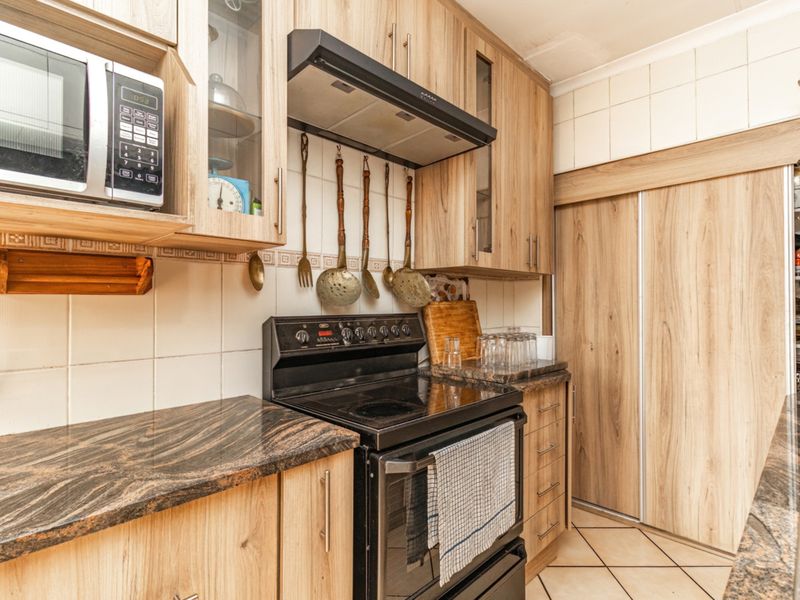A functional kitchen featuring wood-look cabinetry, granite countertops, a built-in microwave, and a freestanding electric stove with an overhead extractor fan.