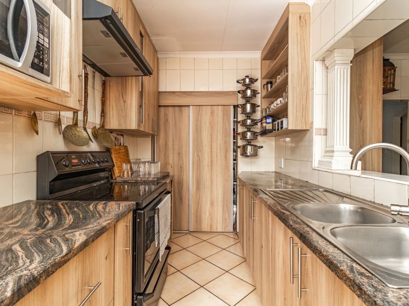 A functional galley-style kitchen featuring wood-finish cabinetry, granite countertops, a built-in oven with extractor, and a double stainless steel sink.