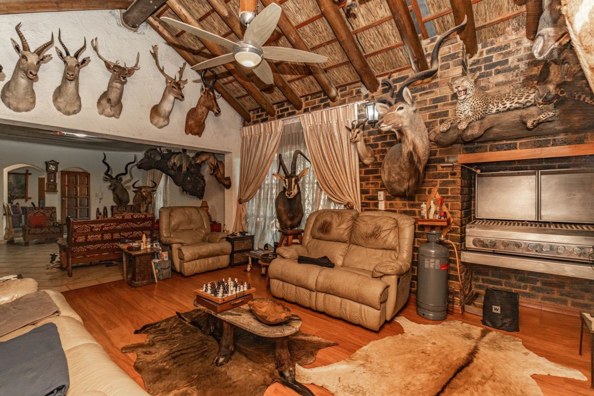 Spacious living area featuring a rustic thatched roof with exposed timber beams, brick fireplace, built-in braai, and laminate flooring.