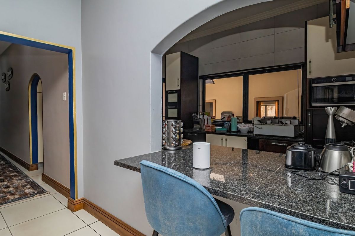 A functional kitchen featuring a granite breakfast bar, built-in oven and microwave, and tiled finishes, connected to a hallway via an arched opening.