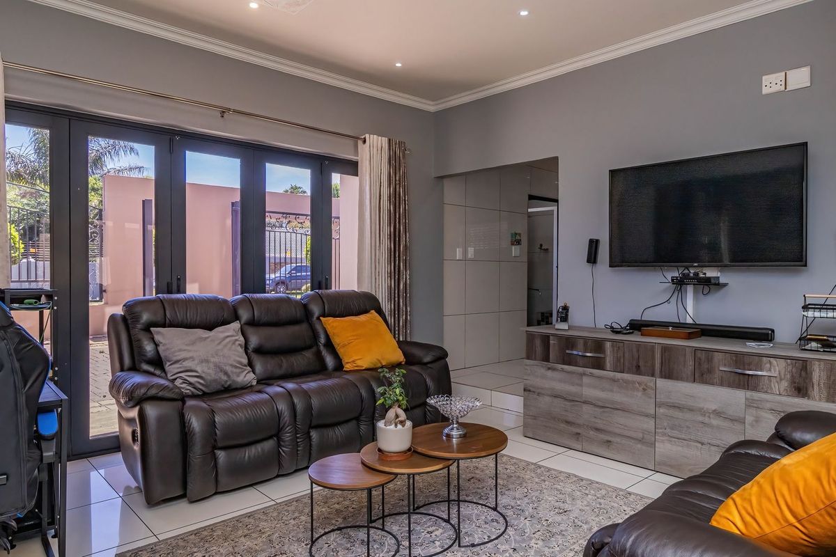 A well-maintained living room featuring tiled flooring, recessed downlighting, and large bi-fold glass doors providing access to the exterior.
