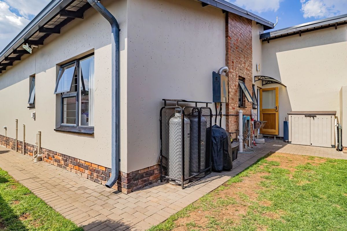 Rear exterior view of the property featuring a paved walkway, gas cylinder storage, external sink, and brick accent wall detailing.
