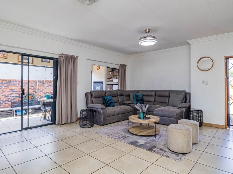 Spacious living room featuring neutral tiled flooring, a ceiling fan, and large sliding glass doors providing direct access to the outdoor patio area.