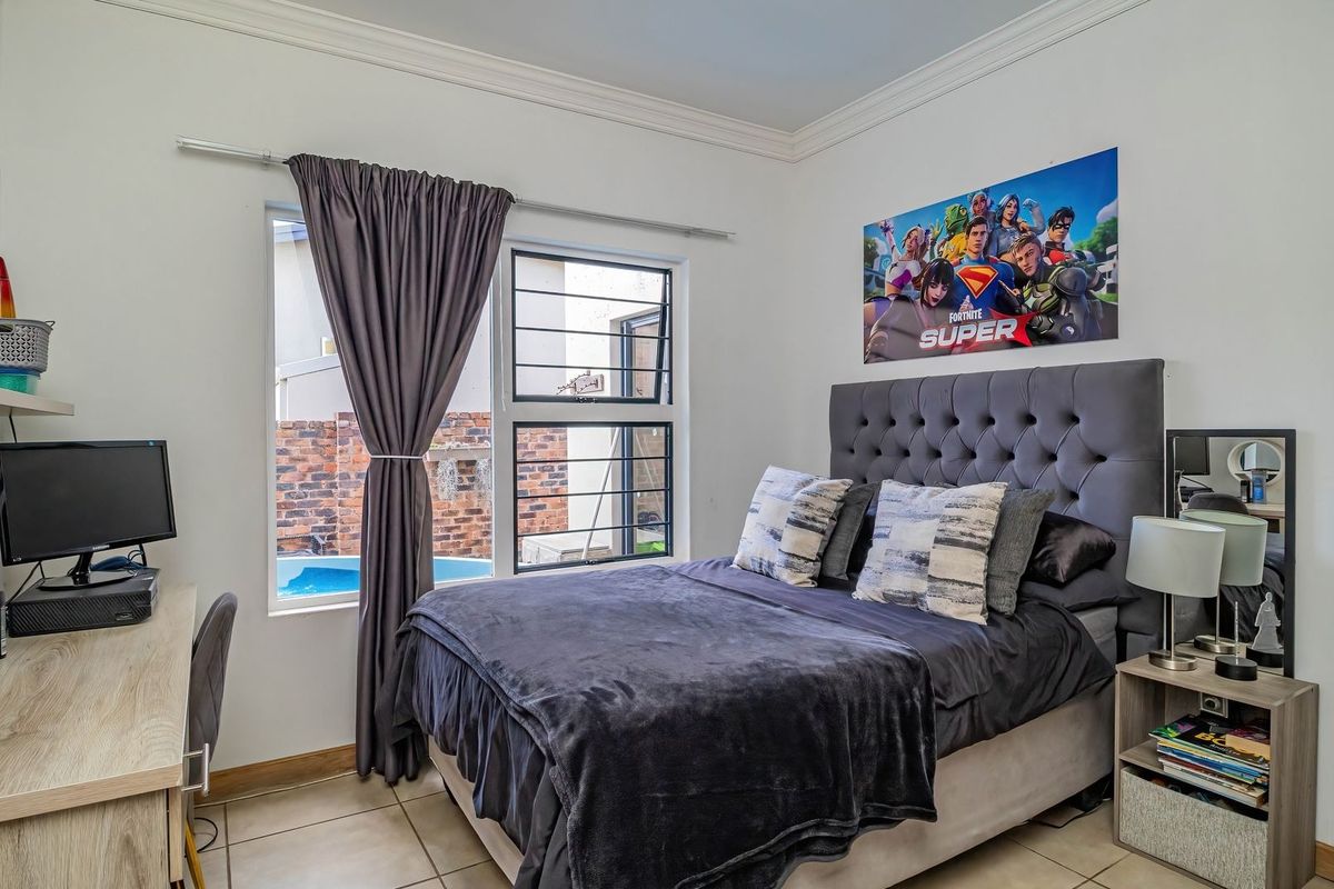 A well-maintained bedroom featuring tiled flooring, a window with security bars, and decorative cornice detailing.