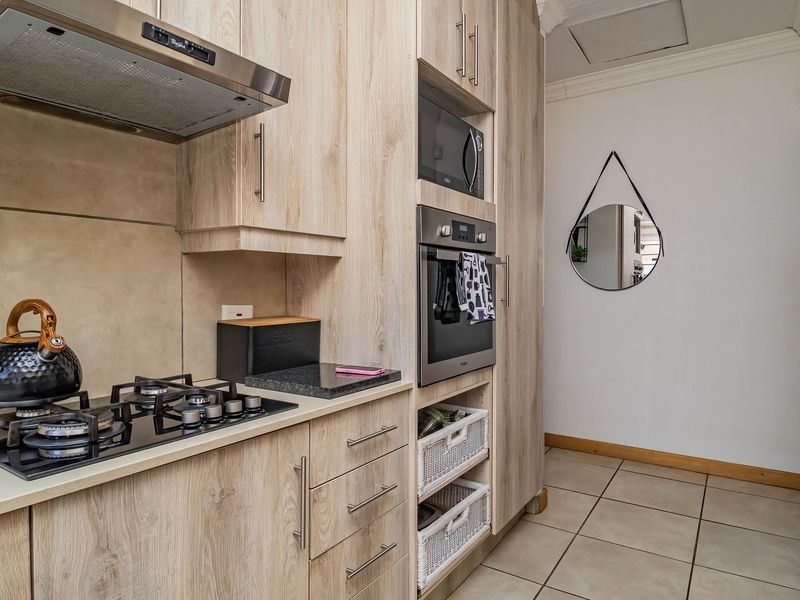 Modern kitchen featuring light wood-grain cabinetry, stone countertops, a gas hob with extractor, and integrated built-in oven and microwave appliances.