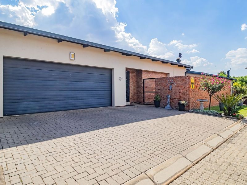 Front elevation of a cluster home featuring a double garage, paved driveway, and a combination of brick and plastered wall finishes.