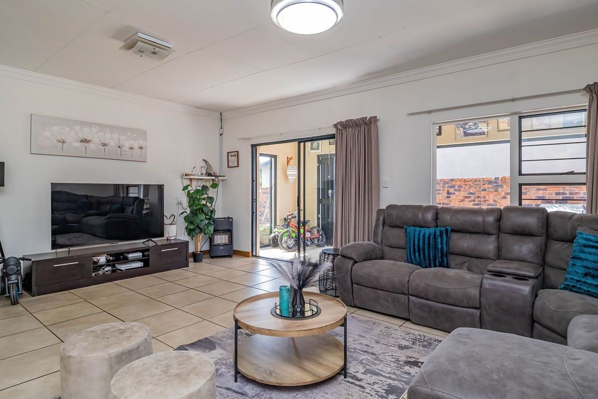 A well-maintained living room featuring tiled flooring, large sliding glass doors providing access to the exterior, and neutral wall finishes.