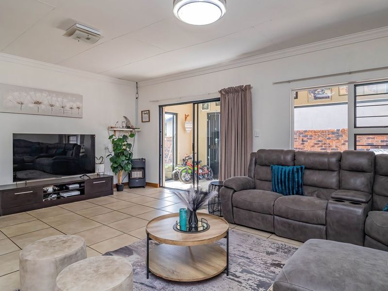 A well-maintained living room featuring tiled flooring, large sliding glass doors providing access to the exterior, and neutral wall finishes.