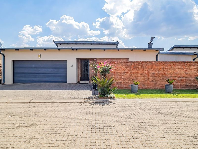 Front elevation of a cluster home featuring a paved driveway, automated garage, and a decorative brick boundary wall.