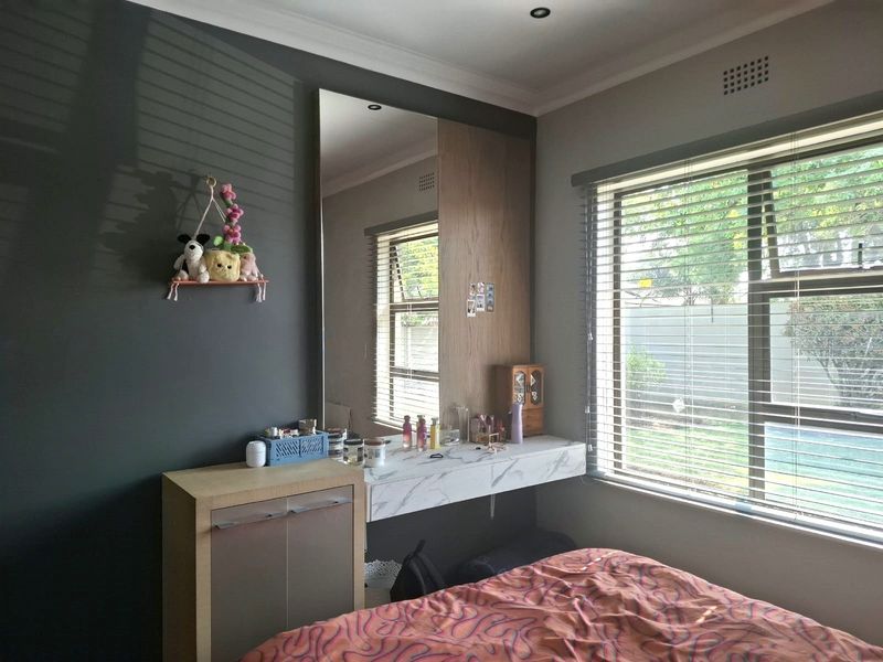 A bedroom featuring a built-in vanity unit with a marble-look countertop, a full-length mirror, and venetian blinds allowing natural light.