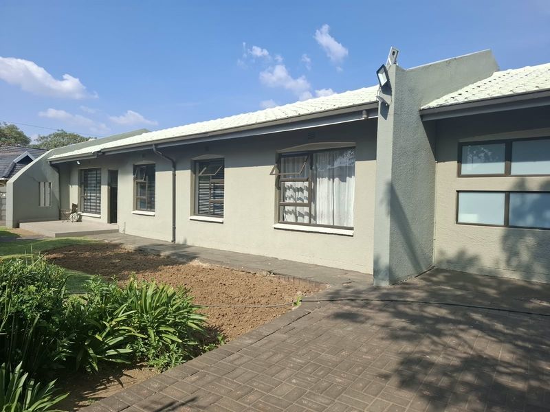 A view of the rear exterior elevation featuring a paved walkway, metal-framed windows with security bars, and a tiled roof.